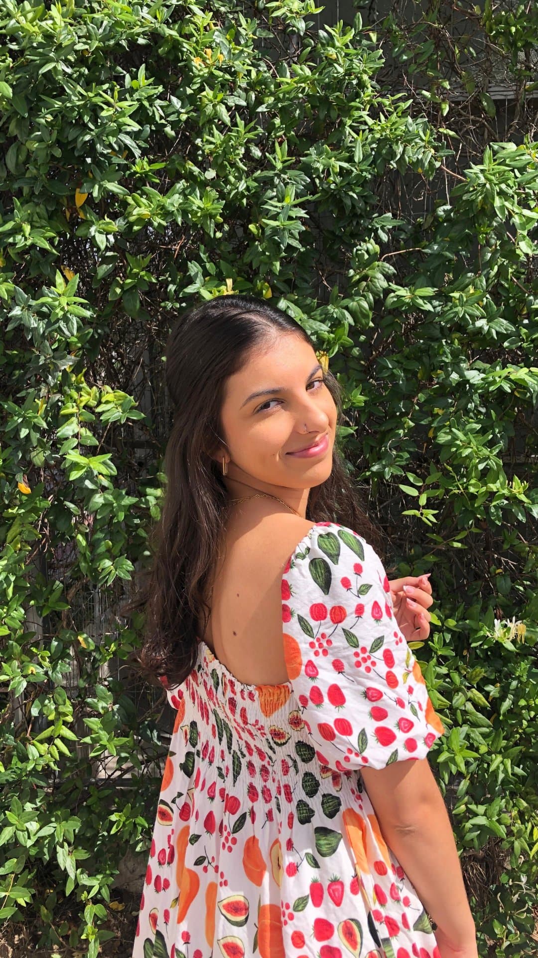 Ana Carolina Calderaro de vestido estampado com frutas, em frente a uma parede de folhagens